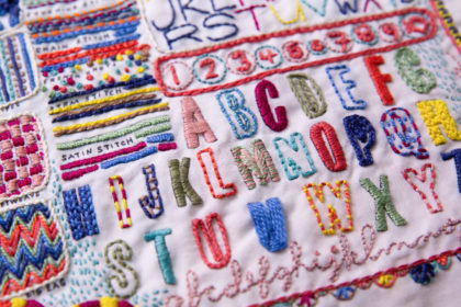 close-up of colorful embroidery - the schoolhouse sampler by Rebecca Ringquist featuring colorful alphabet letters and stitches