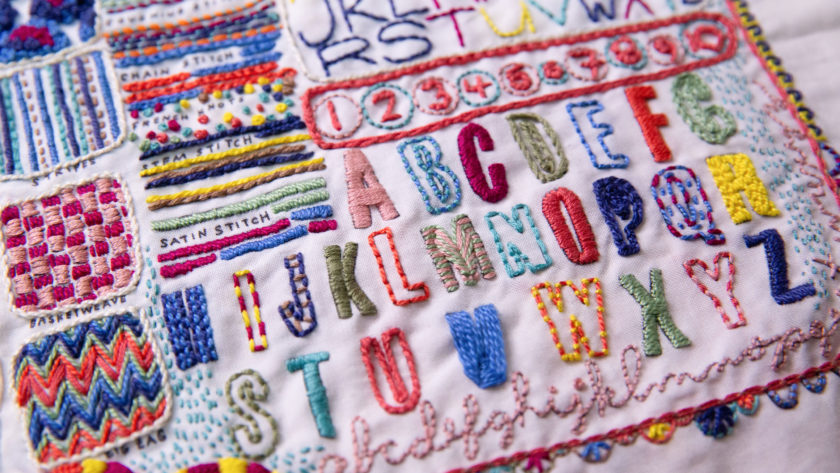 close-up of colorful embroidery - the schoolhouse sampler by Rebecca Ringquist featuring colorful alphabet letters and stitches