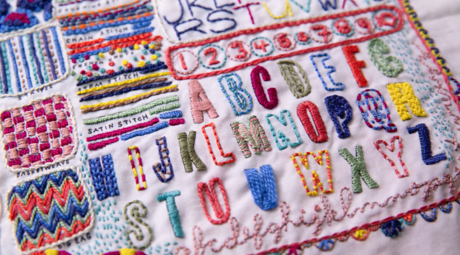 close-up of colorful embroidery - the schoolhouse sampler by Rebecca Ringquist featuring colorful alphabet letters and stitches