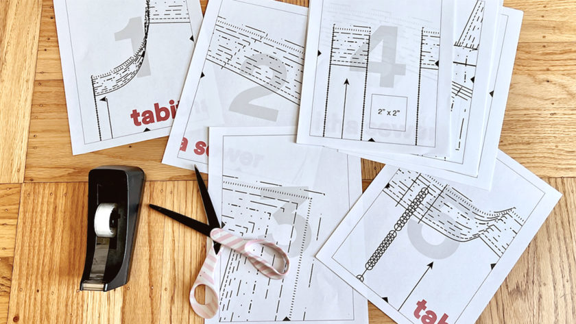 scattered pages of a sewing pattern on a wood floor with scotch tape and scissors