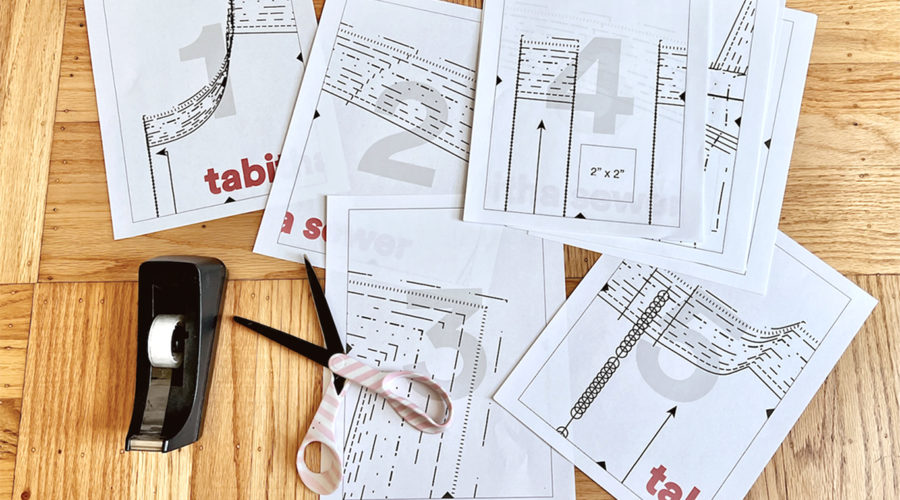 scattered pages of a sewing pattern on a wood floor with scotch tape and scissors