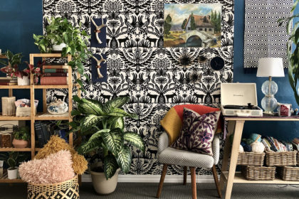 a colorful, textured set for a video that looks like an artist's studio with a black and white patterned wall hanging, wooden book shelves, plants, and chairs