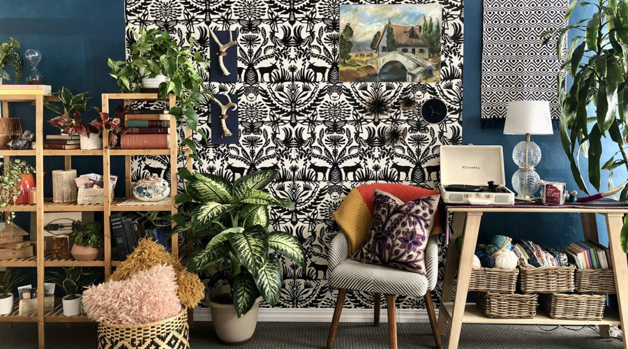 a colorful, textured set for a video that looks like an artist's studio with a black and white patterned wall hanging, wooden book shelves, plants, and chairs