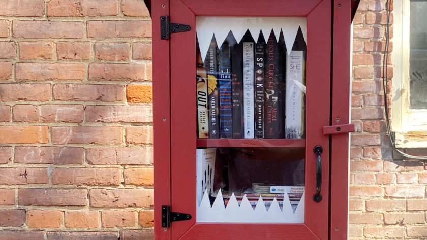 A free library box filled with spooky books and decorated with monster teeth for Halloween