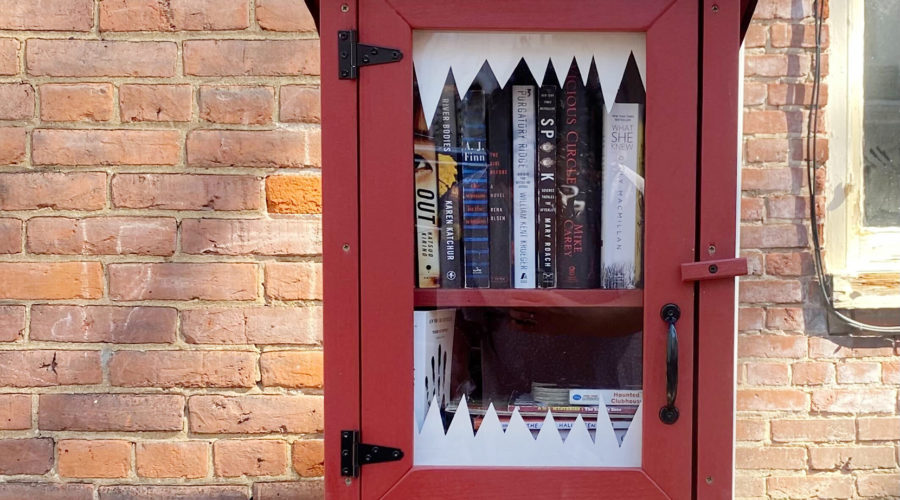 A free library box filled with spooky books and decorated with monster teeth for Halloween