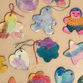 colorfully painted salt dough ornaments scattered on a wooden table - ornament shapes include gingerbread men, hearts, and flowers