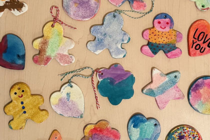 colorfully painted salt dough ornaments scattered on a wooden table - ornament shapes include gingerbread men, hearts, and flowers