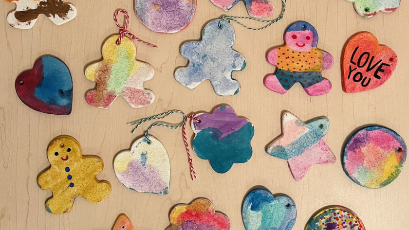 colorfully painted salt dough ornaments scattered on a wooden table - ornament shapes include gingerbread men, hearts, and flowers