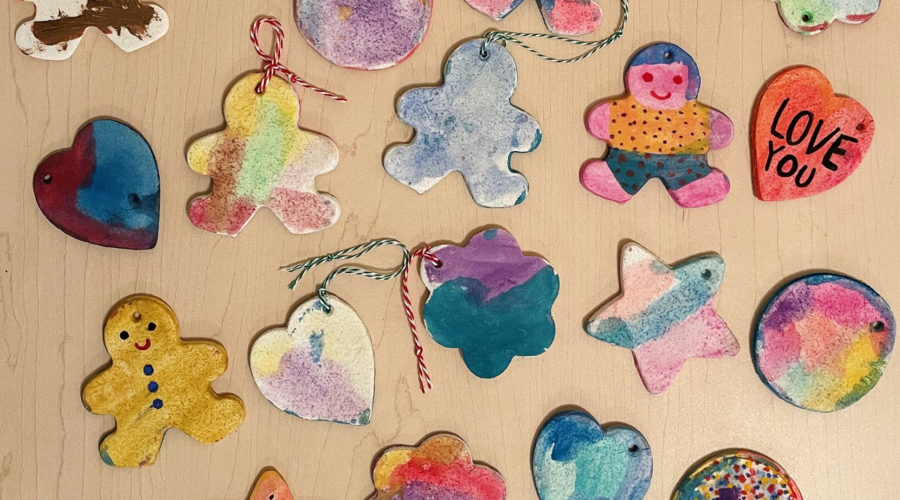colorfully painted salt dough ornaments scattered on a wooden table - ornament shapes include gingerbread men, hearts, and flowers