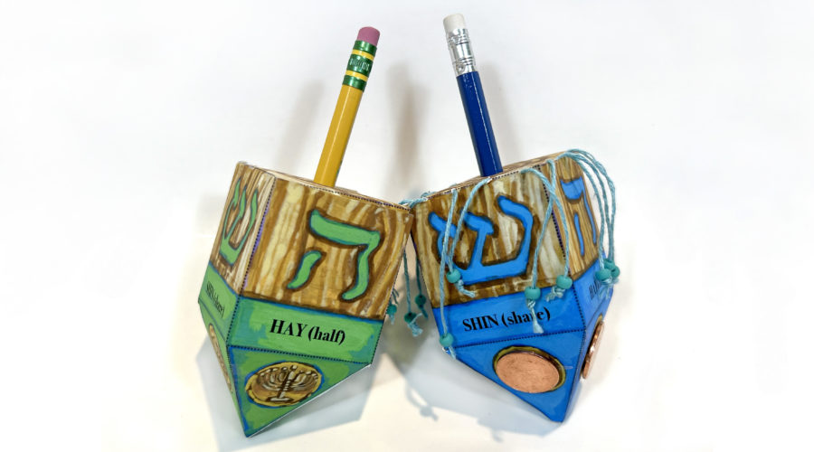 two handmade dreidels made of paper on a white background, one green, one blue, with pencils as handles