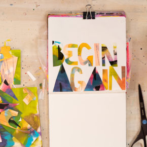 An open sketchbook by abstract painter Abby Houston with painted text that reads "Begin Again"