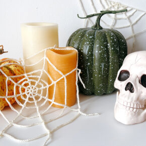 image of a Halloween vignette including crochet spider webs, pumpkins, candles, and a skull