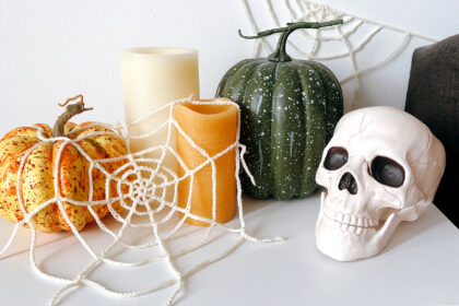 image of a Halloween vignette including crochet spider webs, pumpkins, candles, and a skull