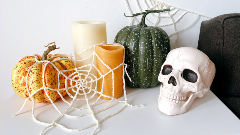 image of a Halloween vignette including crochet spider webs, pumpkins, candles, and a skull