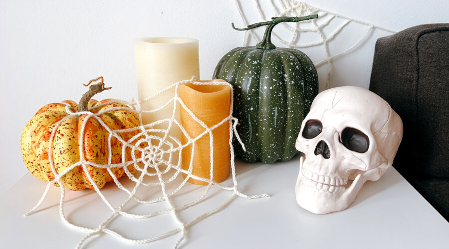 image of a Halloween vignette including crochet spider webs, pumpkins, candles, and a skull