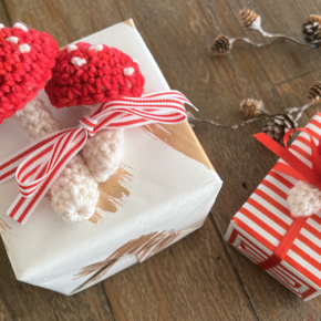 image of small red and white crocheted mushrooms on top of gift boxes warpped in red and white paper