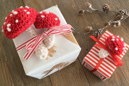 image of small red and white crocheted mushrooms on top of gift boxes warpped in red and white paper