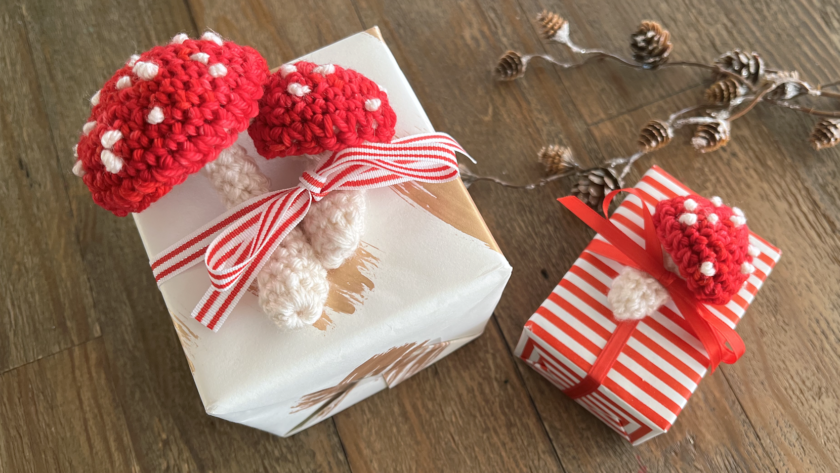 image of small red and white crocheted mushrooms on top of gift boxes warpped in red and white paper