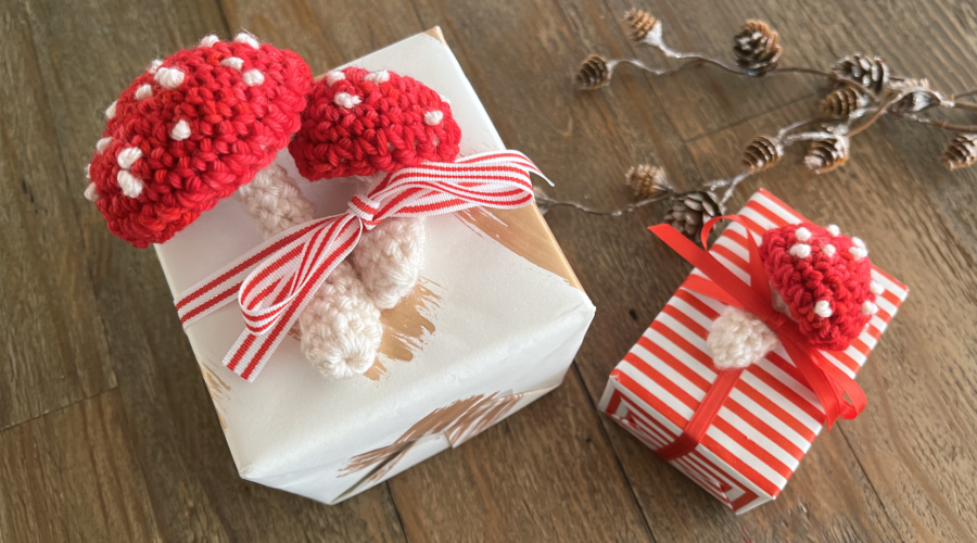 image of small red and white crocheted mushrooms on top of gift boxes warpped in red and white paper