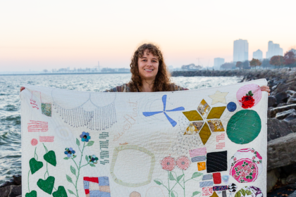 image of a woman holding up her hand stitched quilt by a waterfront