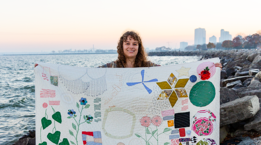 image of a woman holding up her hand stitched quilt by a waterfront
