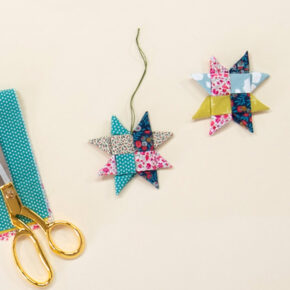 image of 2 woven fabric ornament stars on a cream colored background, styled with a ball of green string, a pair of scissors, and a colorful pile of fabric, to introduce handmade holiday gift ideas