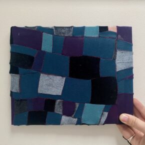 Image of a hand holding a small piece of upycled patchwork in shades of blue and purple.