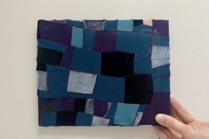 Image of a hand holding a small piece of upycled patchwork in shades of blue and purple.