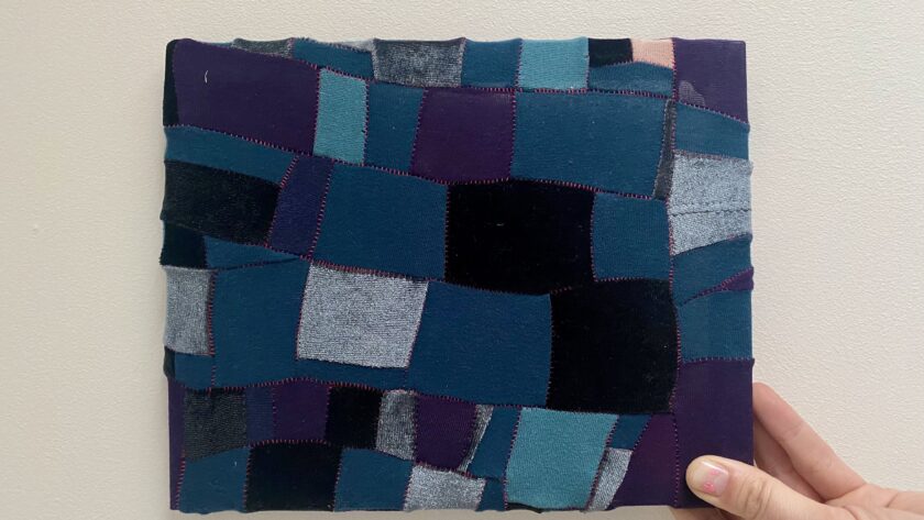Image of a hand holding a small piece of upycled patchwork in shades of blue and purple.