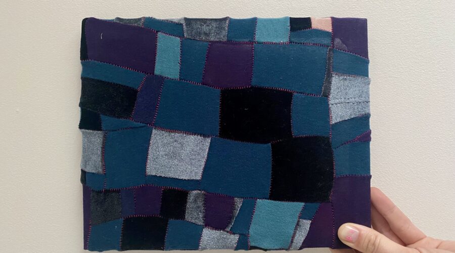 Image of a hand holding a small piece of upycled patchwork in shades of blue and purple.