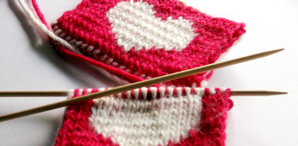close up image of red knitted coasters with a white heart in the middle